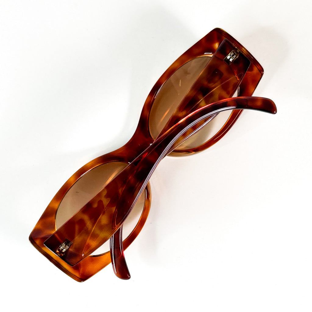 vue de dessus d’une paire de lunettes solaires vintage en acétate écaille, branches croisées sur fond blanc