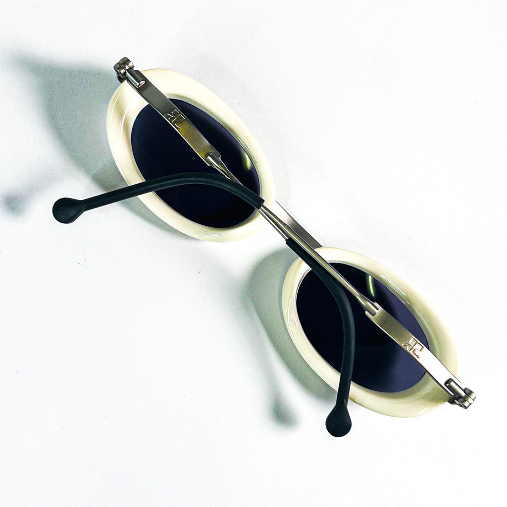 Lunettes de soleil ovales Courrèges ivoire posées à plat vue de trois quarts