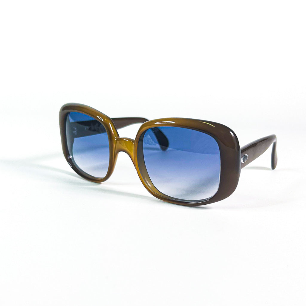 Vue de trois quarts des lunettes de soleil Dior posées à plat, soulignant la brillance de l’acétate et la teinte bleue des verres