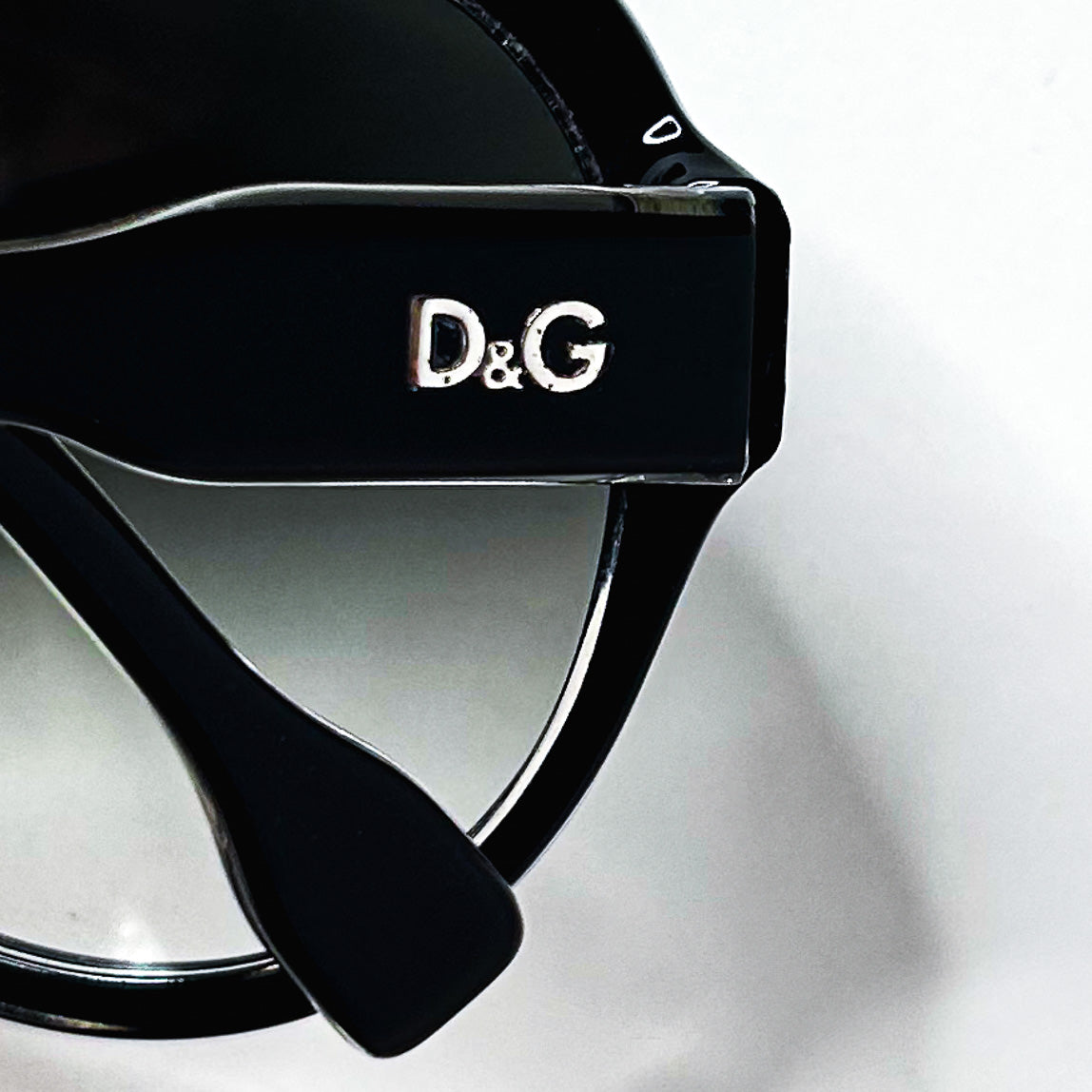 Détail du logo métallique D&G sur la branche des lunettes de soleil noires.