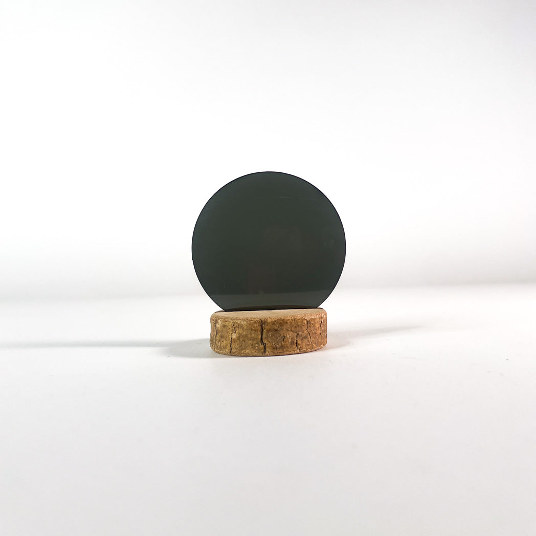 Verre de lunettes de soleil vert foncé uni sur fond blanc et socle en bois