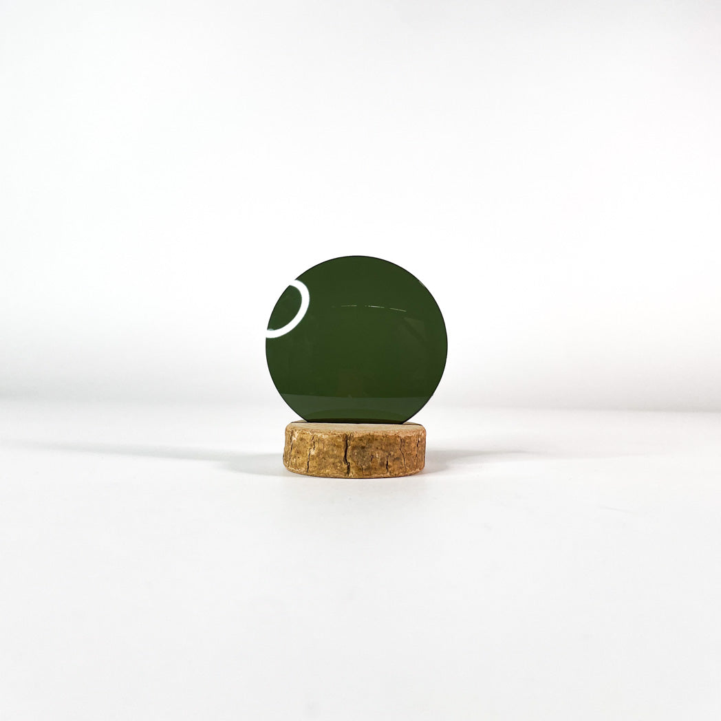 Verre de lunettes de soleil vert foncé uni sur un socle en bois et un fond blanc