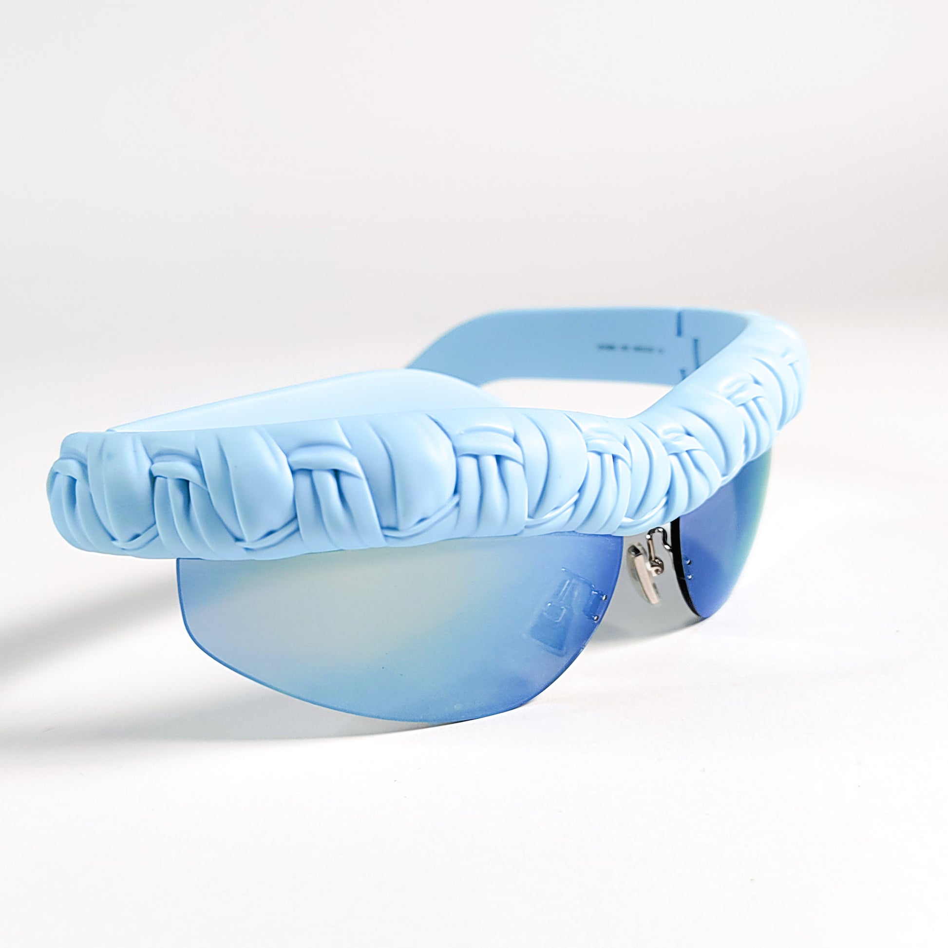 Bottega Veneta BV1209S hero shot 3/4, volume du tressage et reflet bleu glacier du verre miroir.
